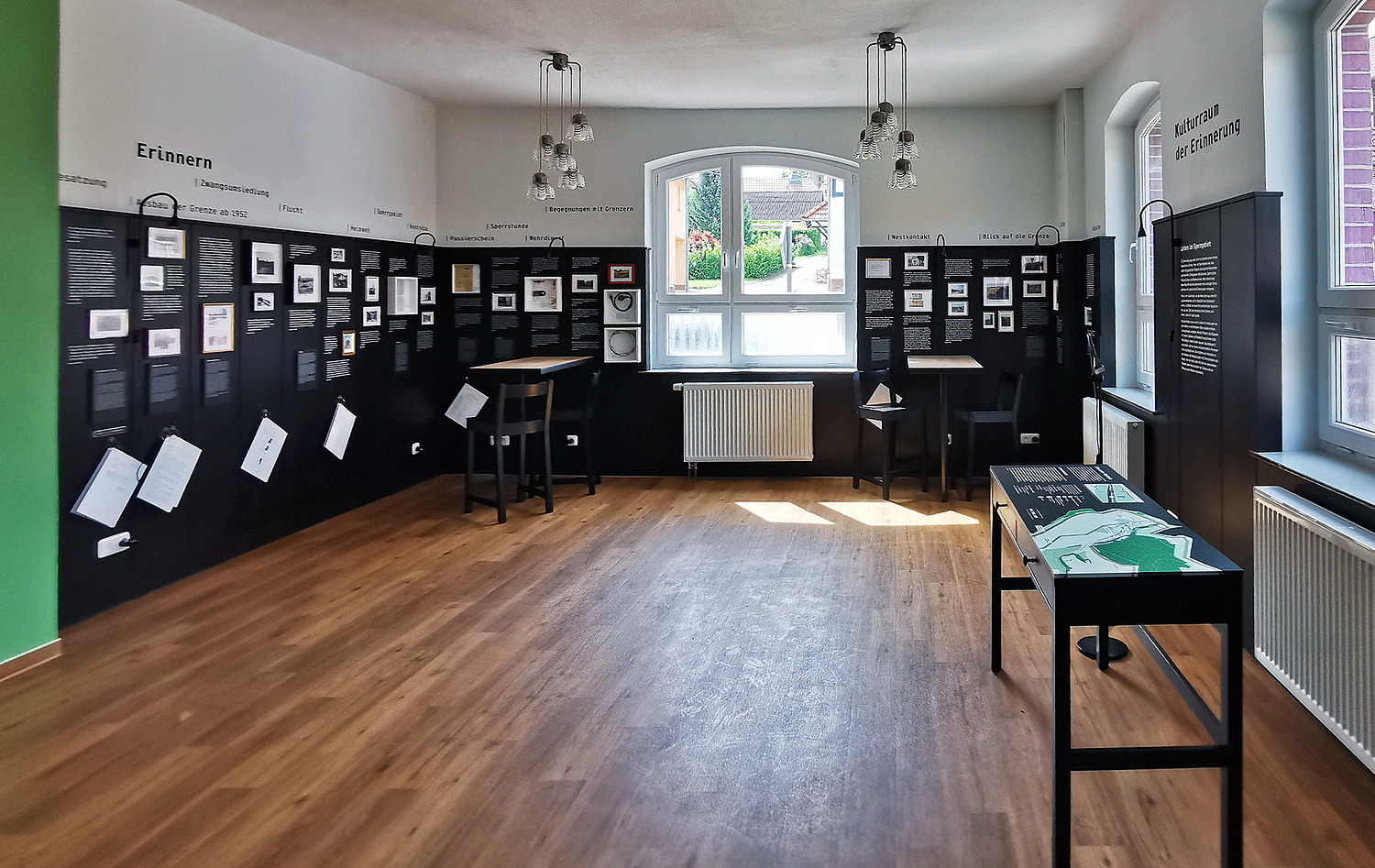 Kulturraum der Erinnerung Glasehausen Gaststube Das Bild zeigt den Blick in die Gaststube mit der umlaufenden Vertäfelung in schwarz und den darauf platzierten Ausstellungselementen. (© Papenfuss | Atelier)