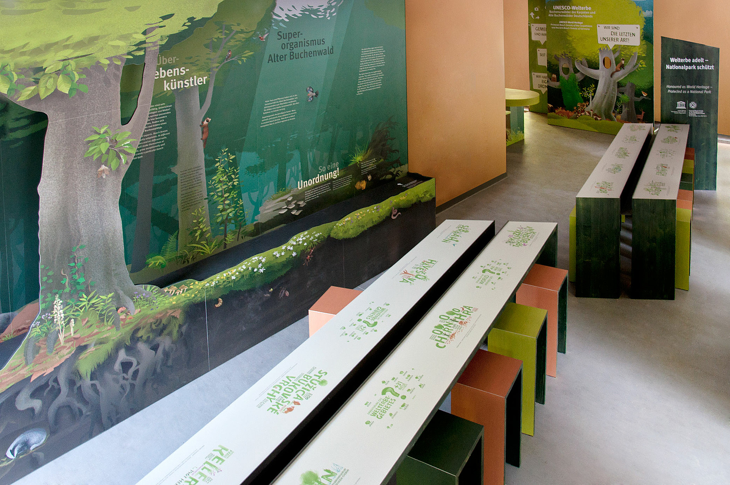 Das Foto zeigt lange Tische und ein Wimmelbild der Ausstellung. (© Papenfuss | Atelier)