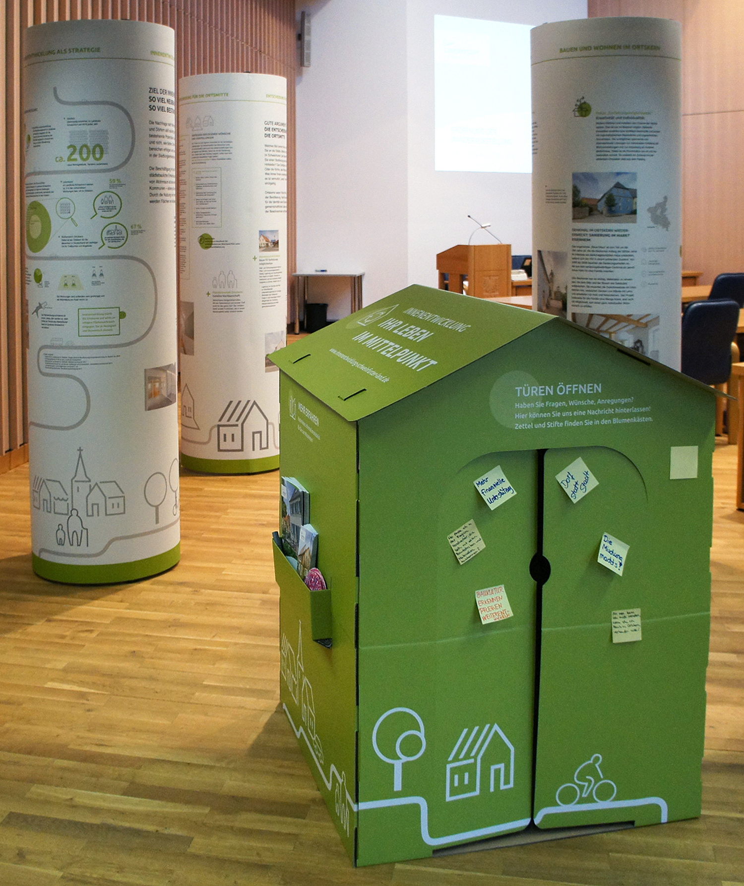 Wanderausstellung Innenarchitektur Kommunikationsdesign Schweinfurt Innentwicklung Die Wanderausstellung, bestehend aus drei Ausstellungssäulen und einem Miniaturhaus als Anlocker, "wandert" innerhalb der Gemeinden des Schweinfurter Landes und kann in verschiedenen öffentlichen Gebäuden gesehen werden. Sie macht auf das Thema und die umfangreichen Angebote des Schweinfurter Landes aufmerksam und verweist auf weiterführende, vertiefende Informationen. (© Papenfuss | Atelier)