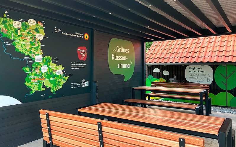 Das Bild zeigt einen Blick in das Grüne Klassenzimmern mit den Bänken unter dem Pavillon sowie einer Karte zum Naturpark.