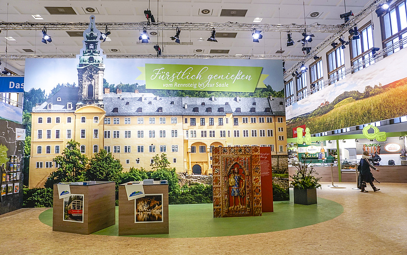 Das Foto zeigt einen Ausschnitt der Thüringen-Präsentation auf der Internationalen Grünen Woche 2019 in Berlin, nämlich eine große Fotowand mit dem Schloss Heidecksburg sowie Informations- und Verkaufsstände.